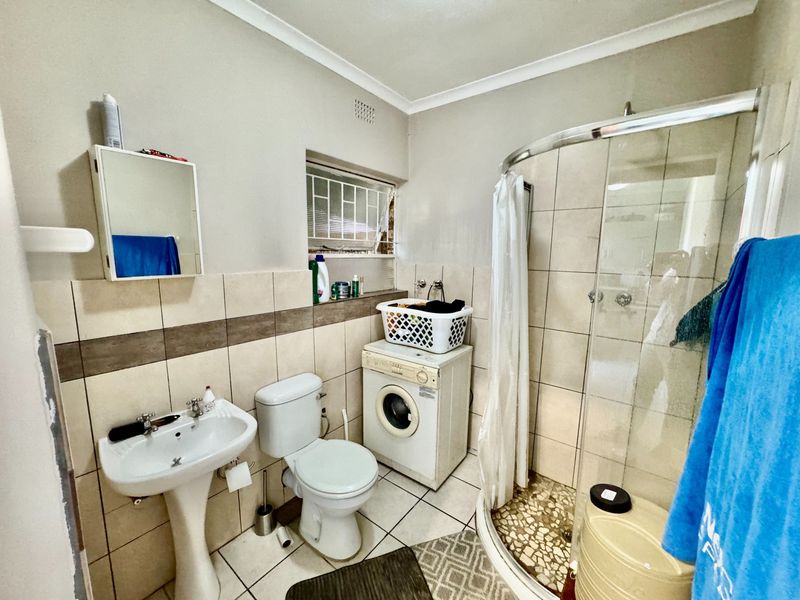 Compact bathroom featuring a pedestal basin, toilet, shower enclosure, and integrated laundry plumbing for a washing machine.