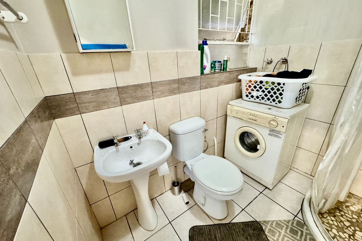 Compact bathroom featuring a pedestal basin, toilet, shower enclosure, and integrated laundry plumbing, finished with neutral wall and floor tiling.
