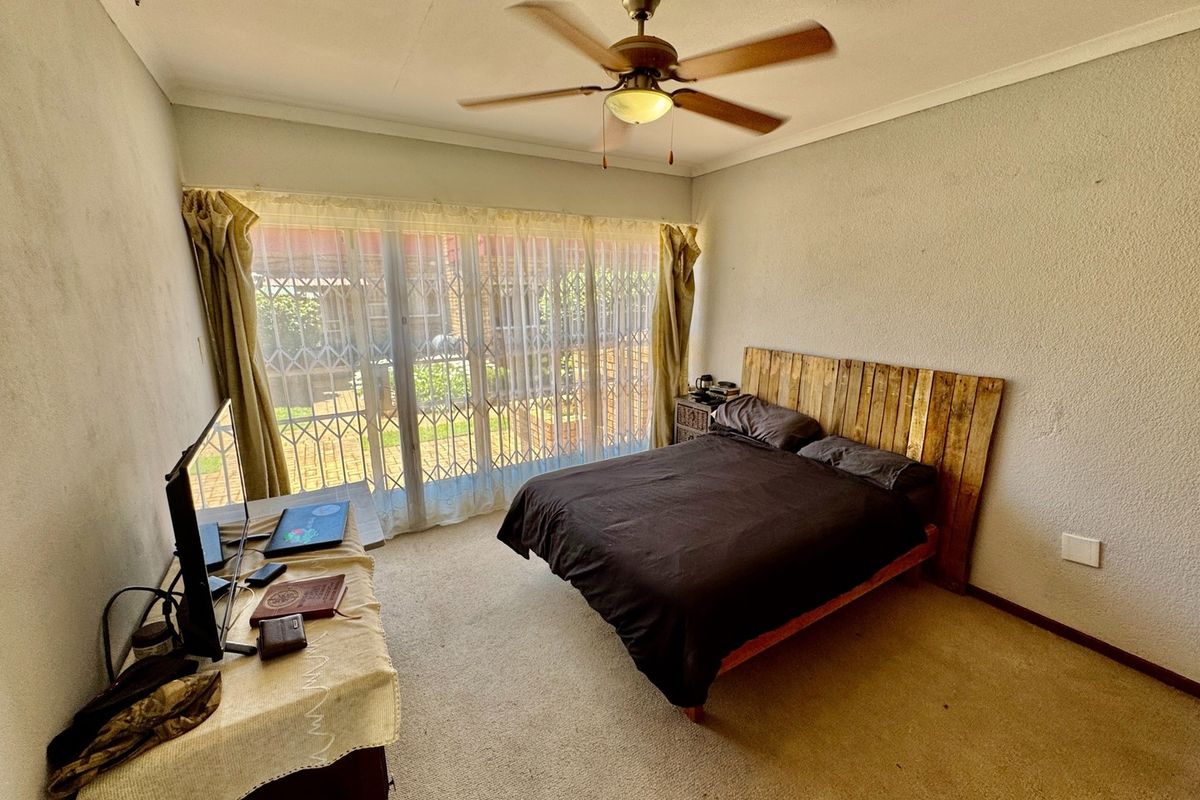 A bedroom featuring a ceiling fan, carpeted flooring, and a sliding glass door with an integrated security gate leading to the exterior.
