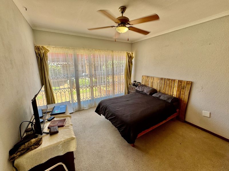 A bedroom featuring a ceiling fan, carpeted flooring, and a sliding glass door with an integrated security gate leading to the exterior.