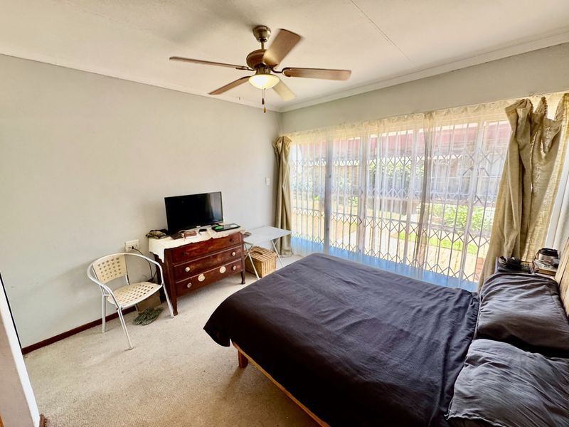 A bedroom featuring a ceiling fan, carpeted flooring, and a large sliding glass door with an integrated security gate leading to the exterior.