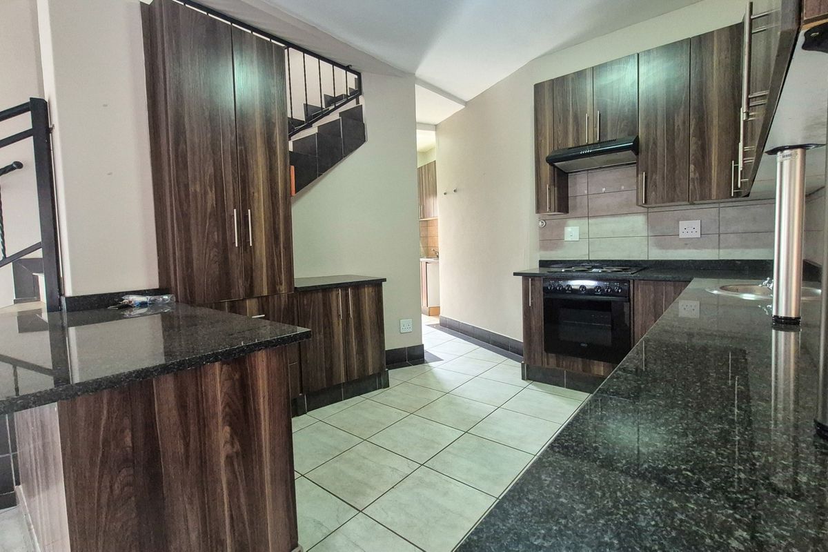 A functional kitchen featuring dark wood cabinetry, granite countertops, built-in oven, gas hob, and tiled flooring, conveniently located adjacent to the staircase.