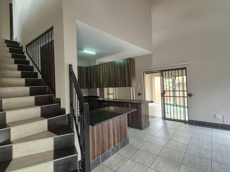Open plan living area featuring a tiled staircase with metal balustrade and a modern kitchen with dark wood cabinetry and granite countertops.