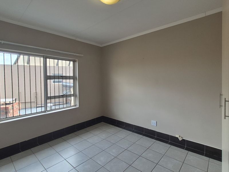 A clean, empty bedroom featuring neutral wall tones, tiled flooring, and a built-in wardrobe, providing a versatile space ready for personalization.