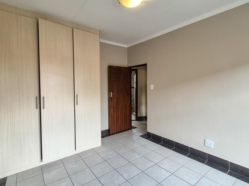 A clean, empty bedroom featuring neutral wall tones, light wood-finish built-in cupboards, and durable tiled flooring with dark skirting.