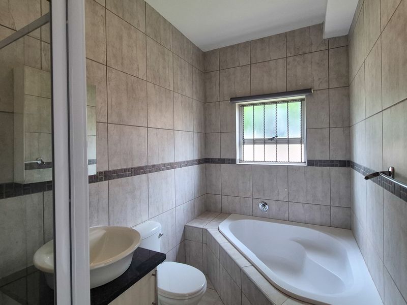 A clean, tiled bathroom featuring a built-in bathtub, a separate shower enclosure, and a vanity with a vessel sink.