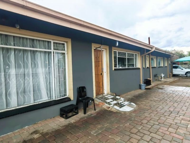 Rear exterior view of the house featuring a paved patio area, security bars on windows, and painted exterior walls.