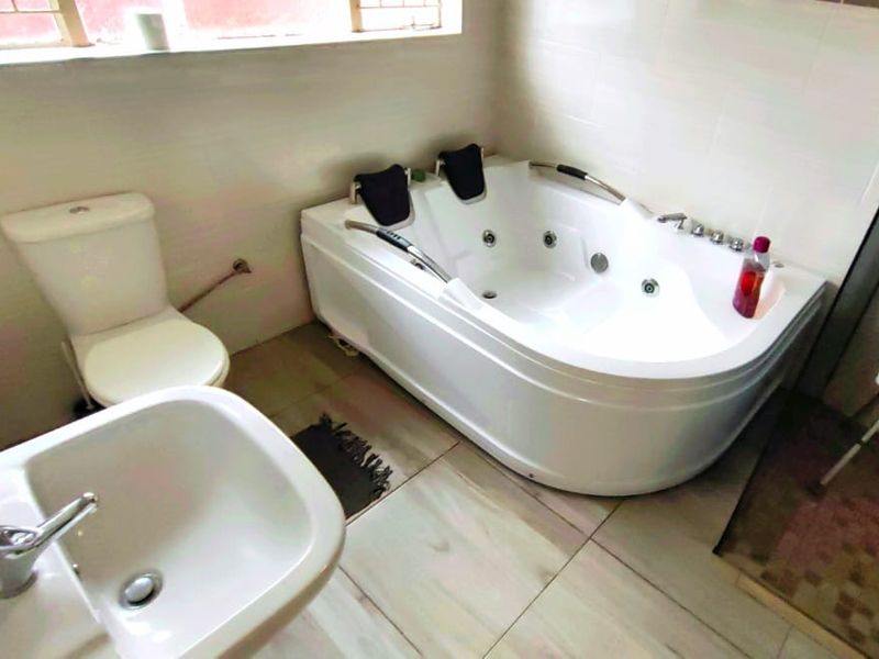 A functional bathroom featuring a corner jacuzzi bathtub, pedestal basin, and toilet with neutral wall and floor tiling.