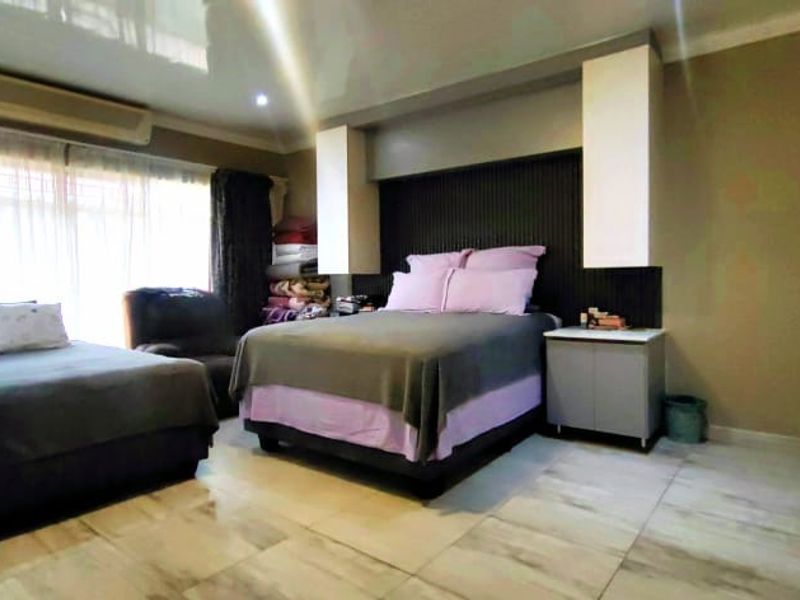 Spacious bedroom featuring tiled flooring, a built-in headboard with integrated cabinetry, and a wall-mounted air conditioning unit.