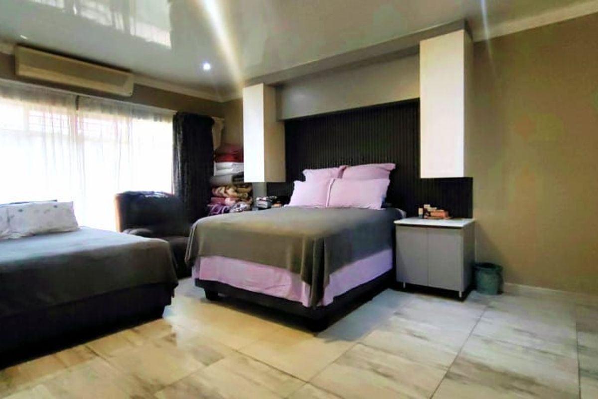 Spacious bedroom featuring tiled flooring, a built-in headboard with integrated cabinetry, and a wall-mounted air conditioning unit.