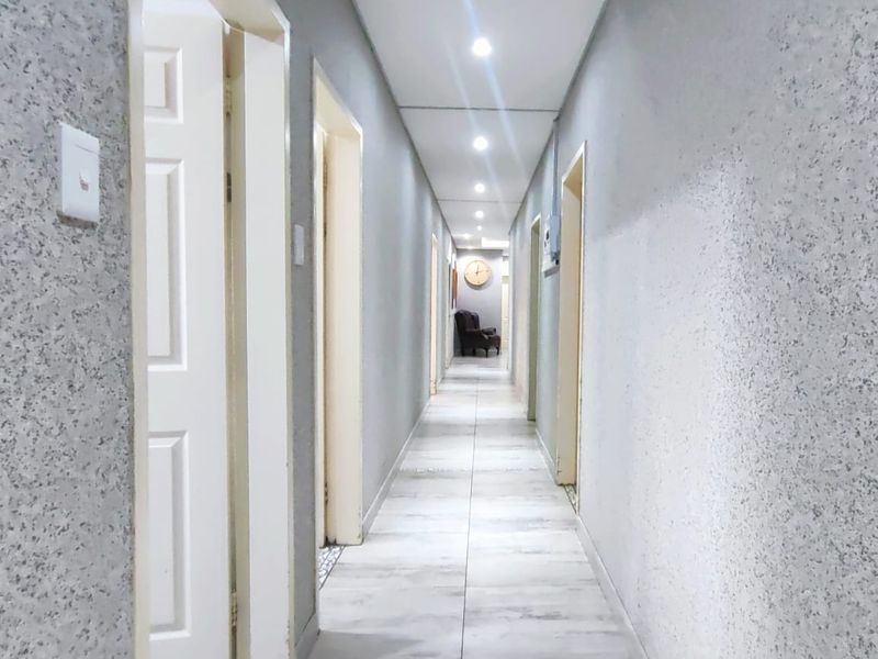 A long, well-lit hallway featuring neutral textured walls and light-toned tiled flooring, providing access to multiple rooms.