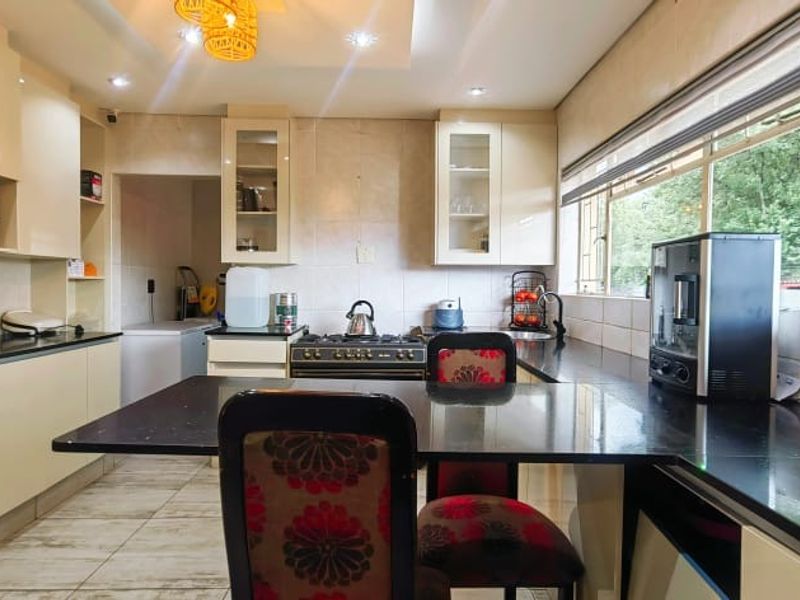 A well-lit kitchen featuring modern cabinetry, granite countertops, a gas stove, and a breakfast nook area with large windows overlooking the garden.