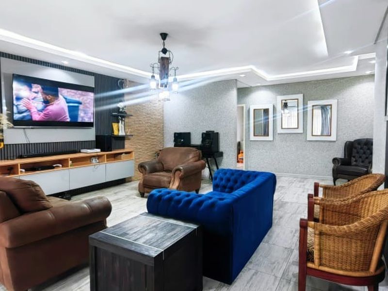 A well-maintained living room featuring modern recessed ceiling lighting, decorative wall paneling, and a built-in media console with tiled flooring.
