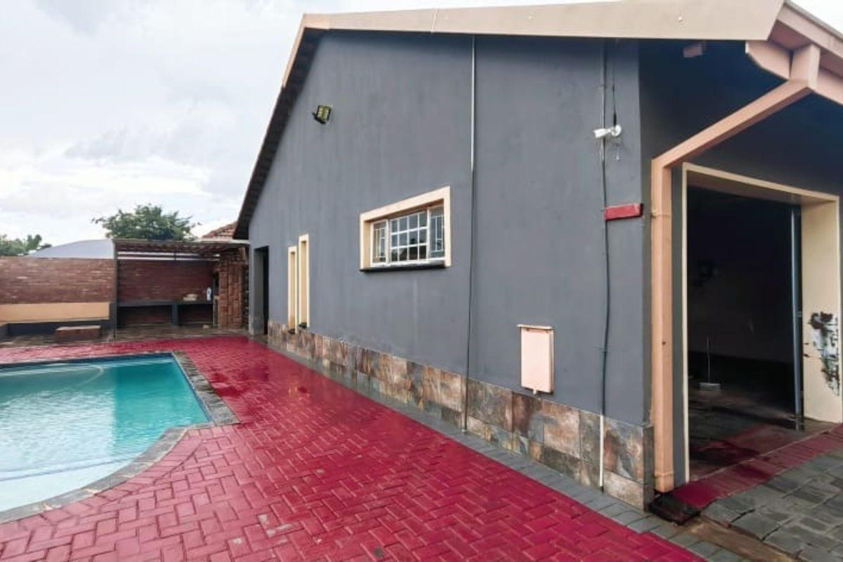 Rear exterior view featuring a swimming pool, paved patio area, and a built-in braai, set against the side elevation of the house.