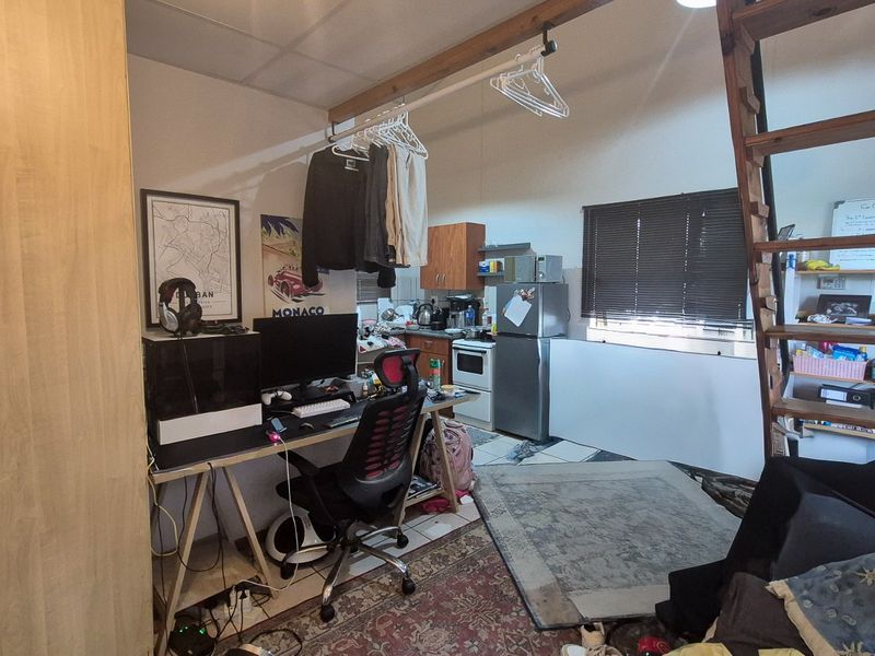 Open-plan apartment living area featuring a compact kitchen with built-in cabinetry, appliances, and a wooden staircase leading to a loft level.