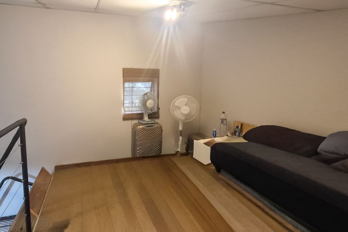 A loft-style bedroom area featuring timber flooring and a metal balustrade overlooking the lower level, requiring cosmetic updates to improve the overall finish.