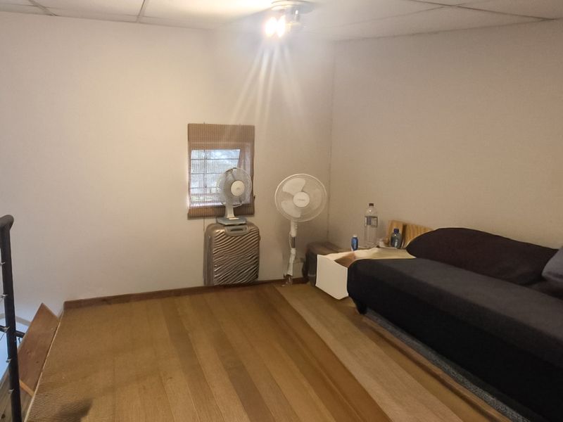 A loft-style bedroom area featuring timber flooring and a metal balustrade overlooking the lower level, requiring cosmetic updates to improve the overall finish.