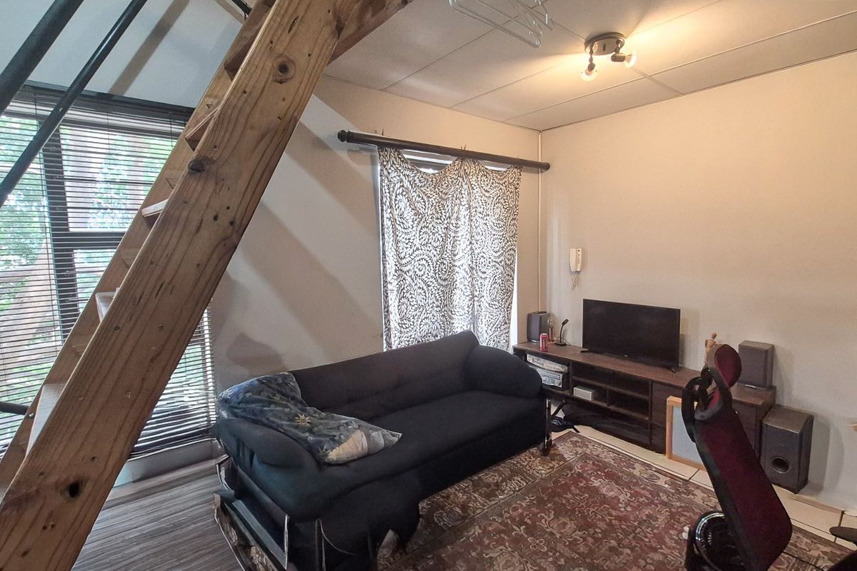 A living room area featuring a prominent wooden staircase, large window with blinds, and neutral wall finishes.