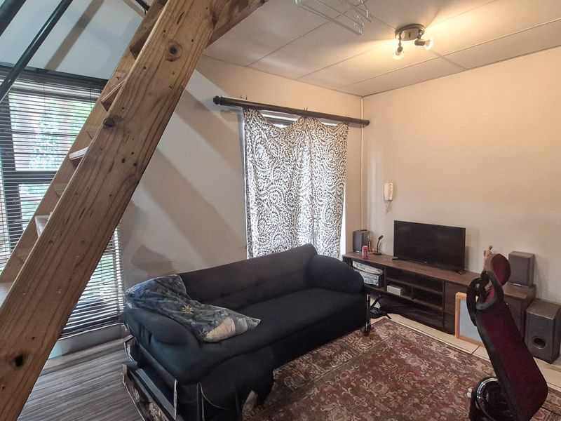 A living room area featuring a prominent wooden staircase, large window with blinds, and neutral wall finishes.