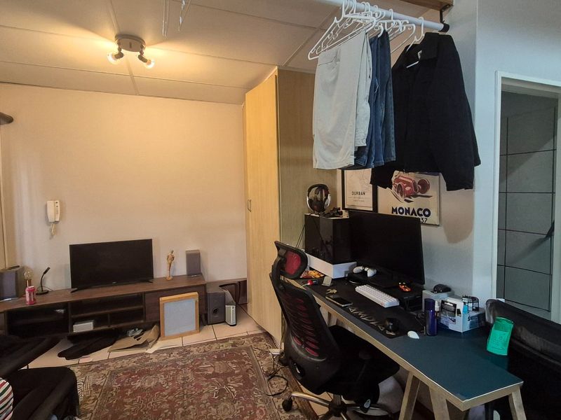 A functional living area featuring tiled flooring and a built-in wardrobe, currently utilized as a combined lounge and workspace.