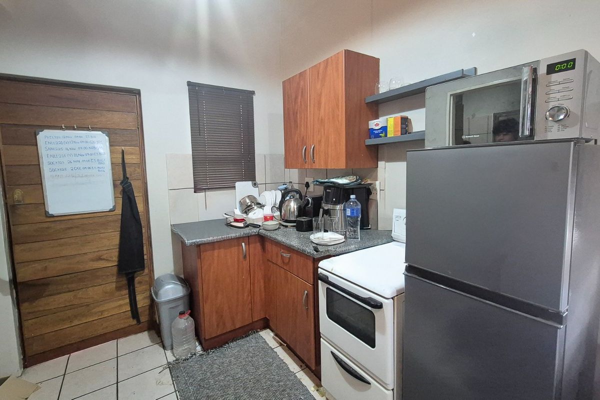 Compact kitchen featuring laminate cabinetry, tiled backsplash, and built-in oven, providing a functional workspace with tiled flooring and a window with venetian blinds.