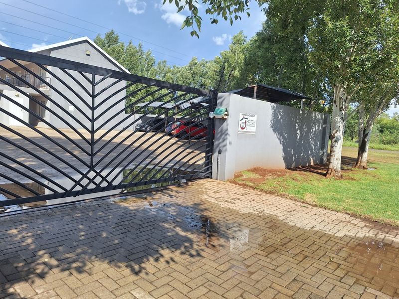 Front entrance view of the apartment complex featuring a secure electric gate, perimeter wall, and paved driveway with covered parking.