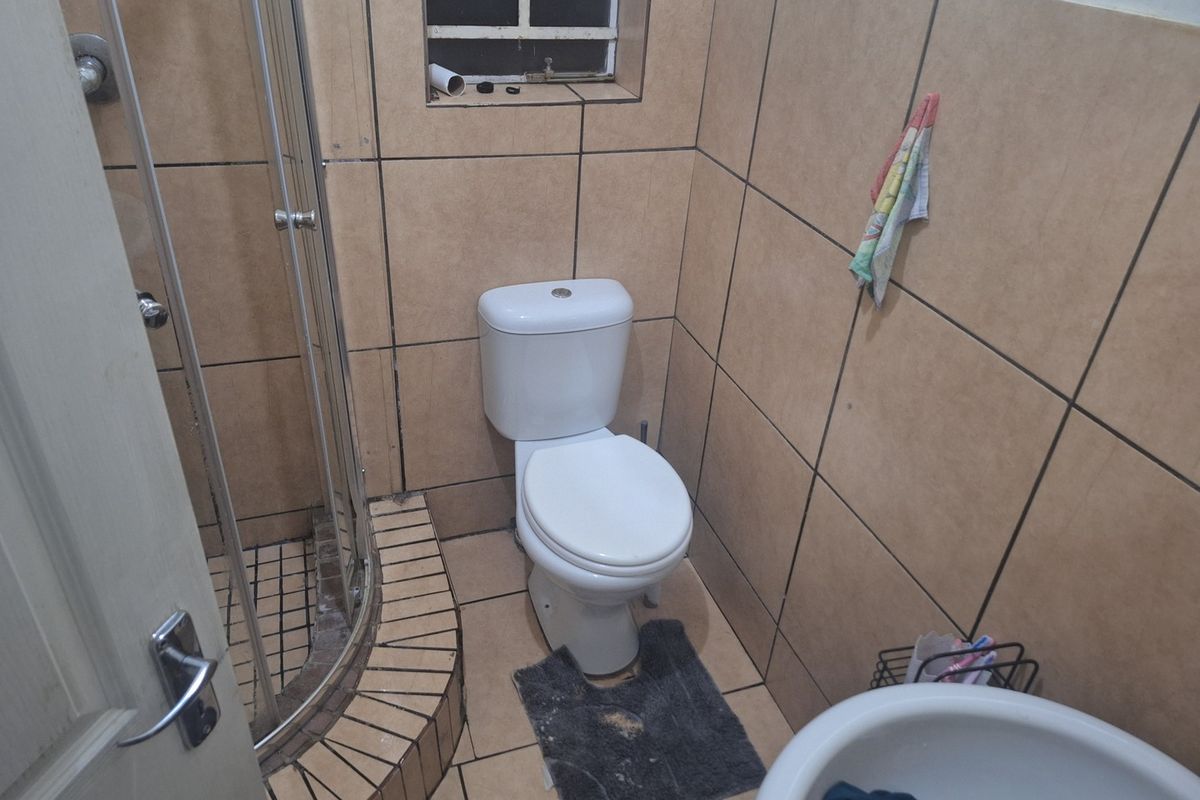 A compact bathroom featuring a corner shower enclosure, standard toilet, and pedestal basin with full-height wall tiling.