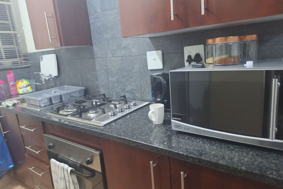 A functional kitchen featuring dark wood cabinetry, granite countertops, a gas hob, and a built-in oven with a tiled backsplash.