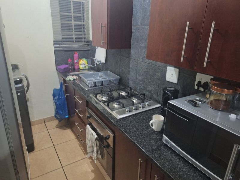 A functional kitchen featuring dark wood cabinetry, granite countertops, a gas hob, and an under-counter oven with tiled backsplash and flooring.