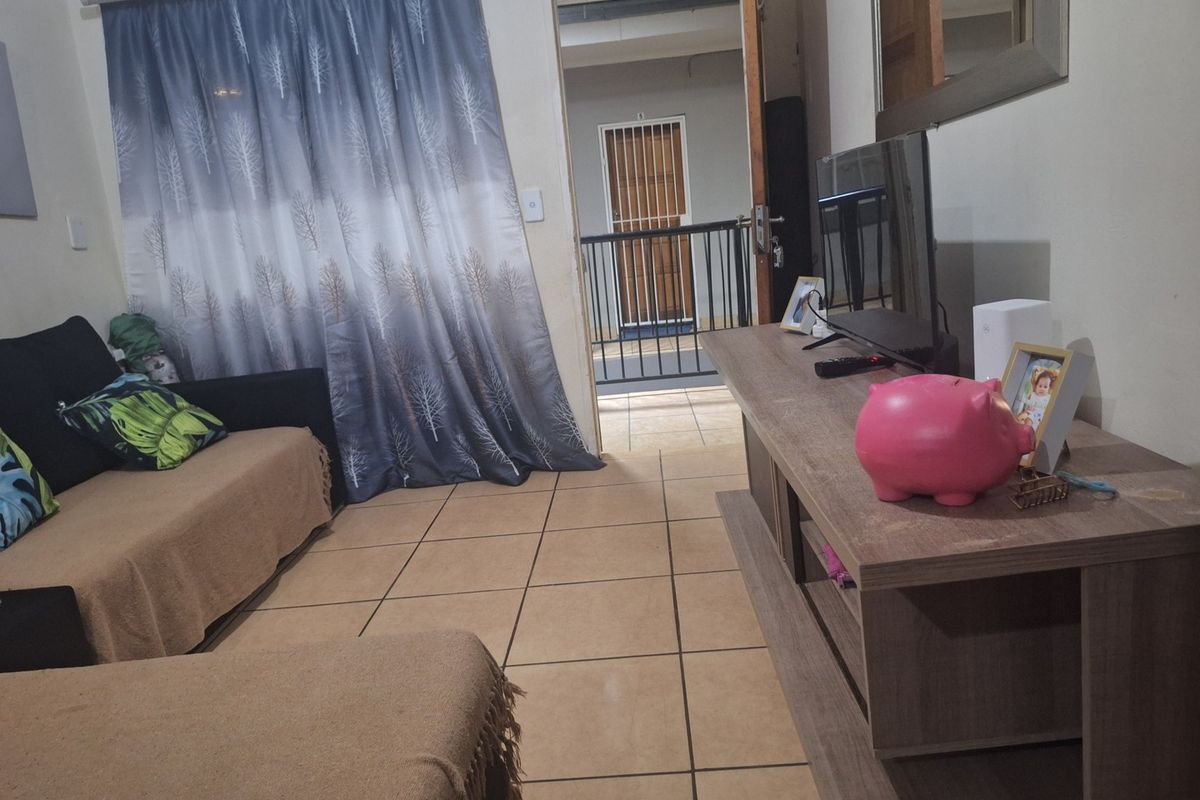 A living room area featuring tiled flooring and direct access to an external balcony through a doorway with a security gate.