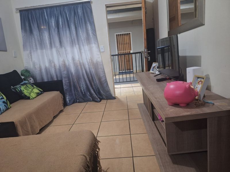 A living room area featuring tiled flooring and direct access to an external balcony through a doorway with a security gate.