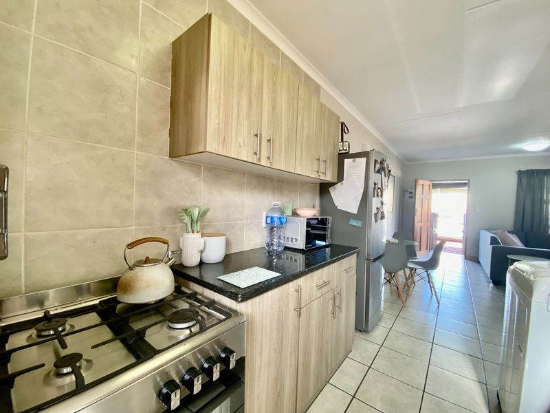 Open plan kitchen featuring light wood cabinetry, granite countertops, and a gas stove, flowing into a tiled living and dining area.