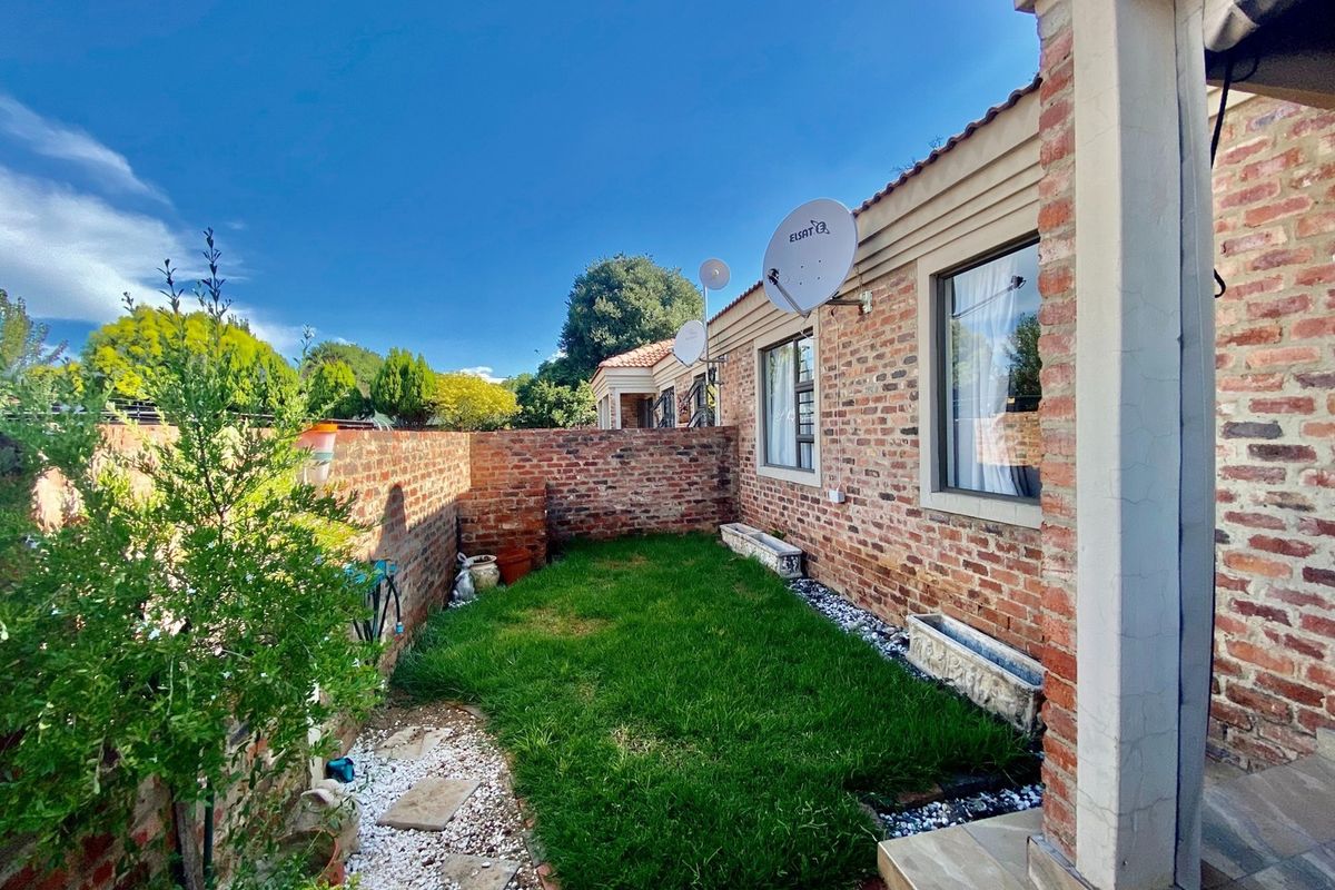 A private rear garden area featuring an exposed brick facade, a small lawn, and a paved patio section.