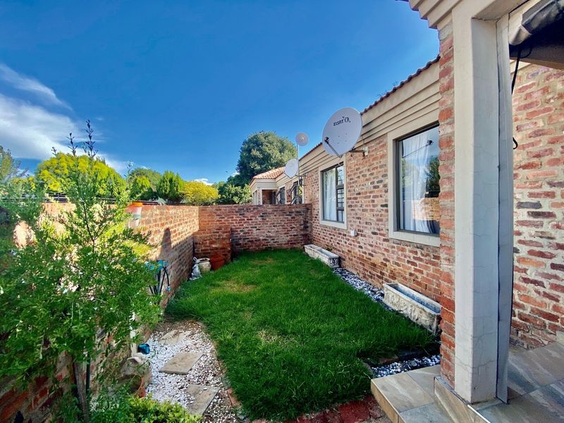 A private rear garden area featuring an exposed brick facade, a small lawn, and a paved patio section.