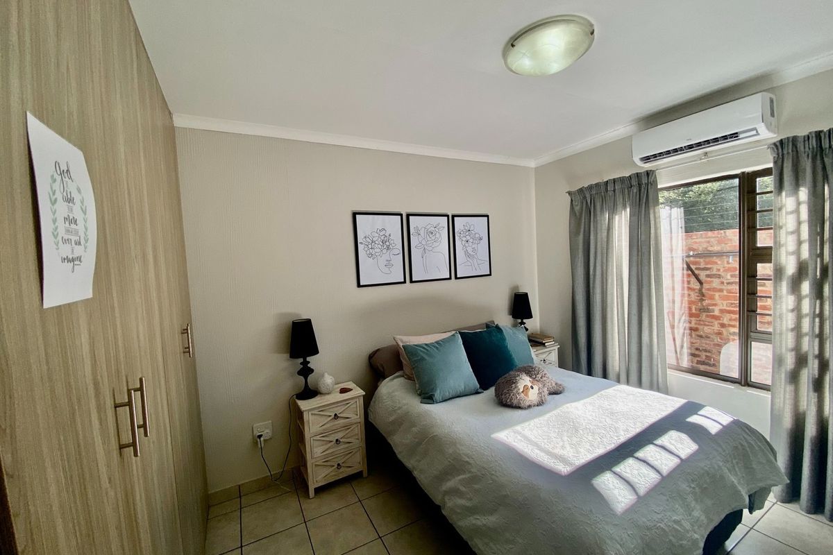 A well-maintained bedroom featuring built-in cupboards, tiled flooring, and a wall-mounted split-system air conditioner for climate control.