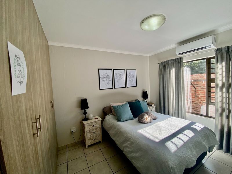 A well-maintained bedroom featuring built-in cupboards, tiled flooring, and a wall-mounted split-system air conditioner for climate control.