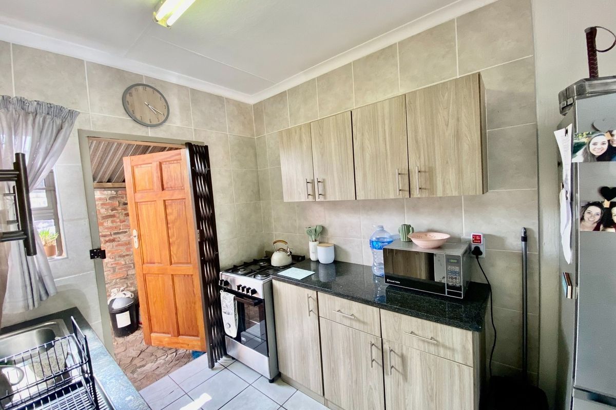 A functional kitchen featuring wood-look cabinetry, granite countertops, a gas stove, and tiled finishes, with direct access to an outdoor area.