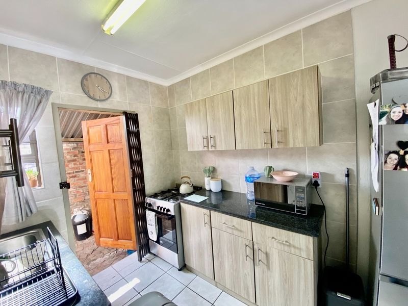 A functional kitchen featuring wood-look cabinetry, granite countertops, a gas stove, and tiled finishes, with direct access to an outdoor area.