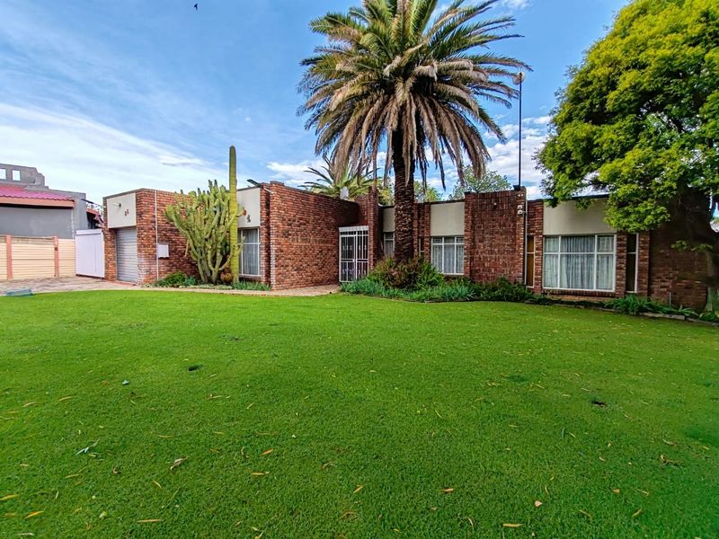 A well-maintained single-story face brick house featuring a large front lawn, mature palm tree, and integrated garage.