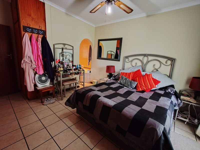 A bedroom featuring tiled flooring, a ceiling fan, and a built-in cupboard, with an arched doorway leading to an adjoining space.