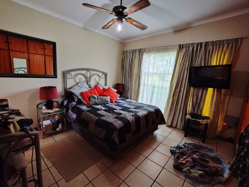 A functional bedroom featuring tiled flooring, a ceiling fan, and built-in cupboards, offering a comfortable and practical living space.