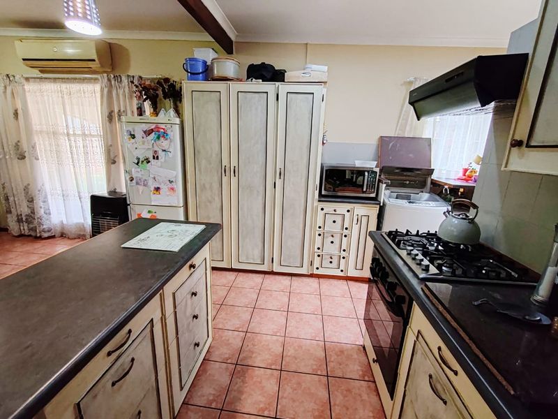 A functional kitchen featuring a central island, gas hob with extractor, and ample built-in cabinetry, finished with tiled flooring and neutral wall tones.