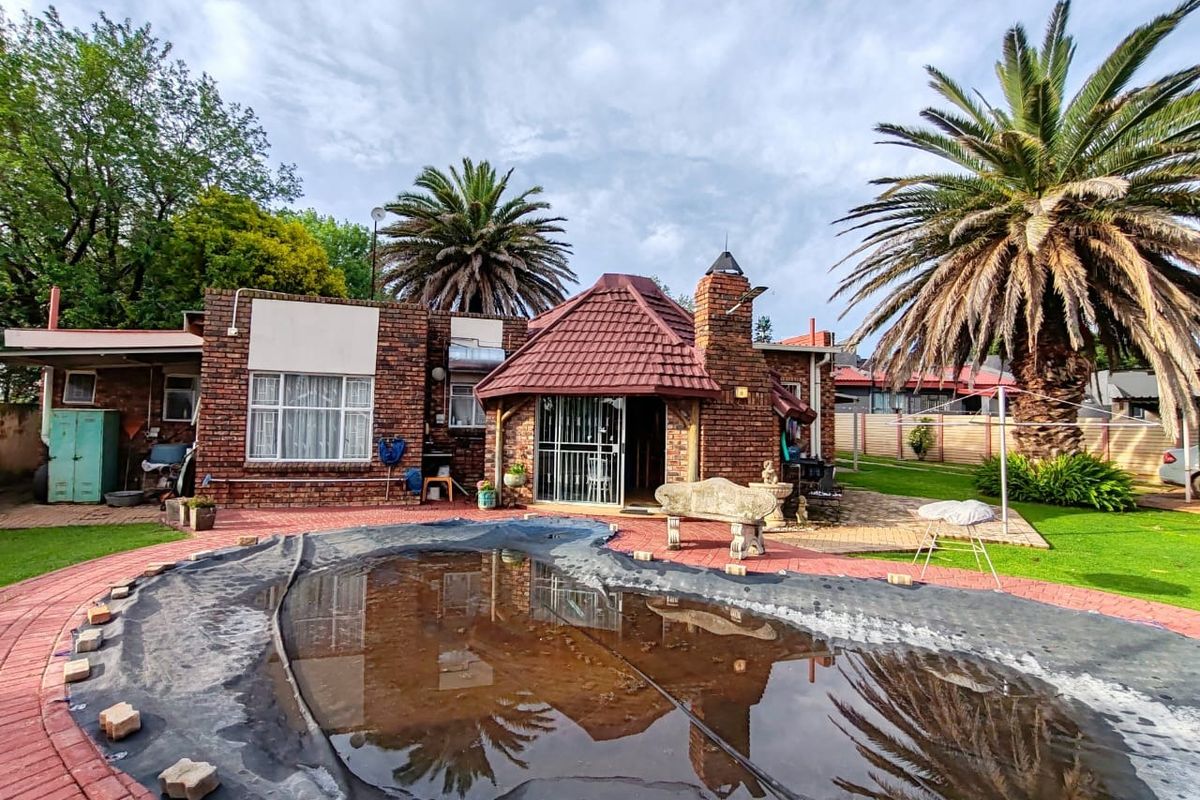 Rear view of a brick house featuring a paved patio area and a swimming pool with a cover.