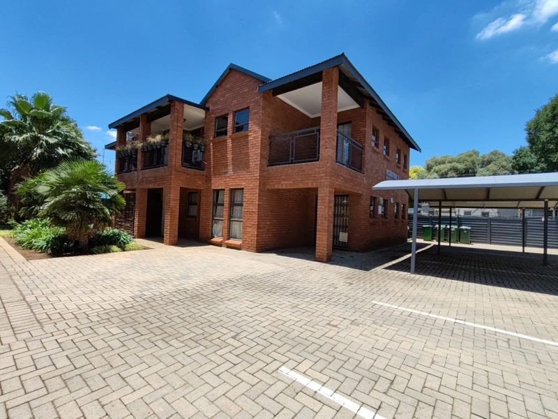 Front view of a face brick apartment building featuring paved parking areas, covered carports, and upper-level balconies.