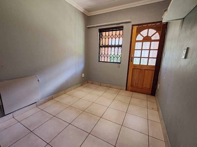 An empty bedroom featuring tiled flooring, a timber door with glass panels, and a window fitted with a security gate.