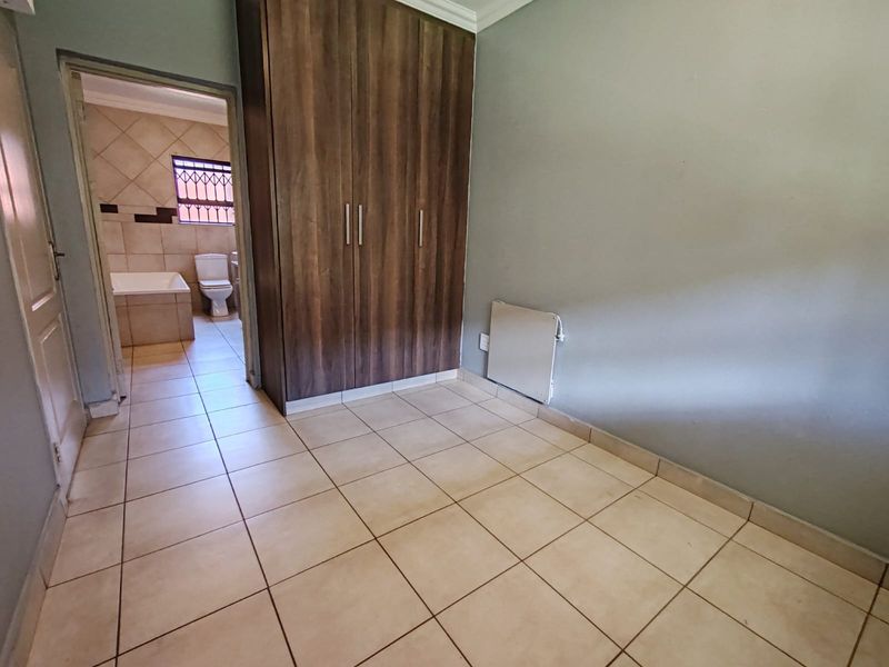 A bedroom featuring tiled flooring and built-in wooden cupboards, with an adjacent en-suite bathroom visible through the doorway.