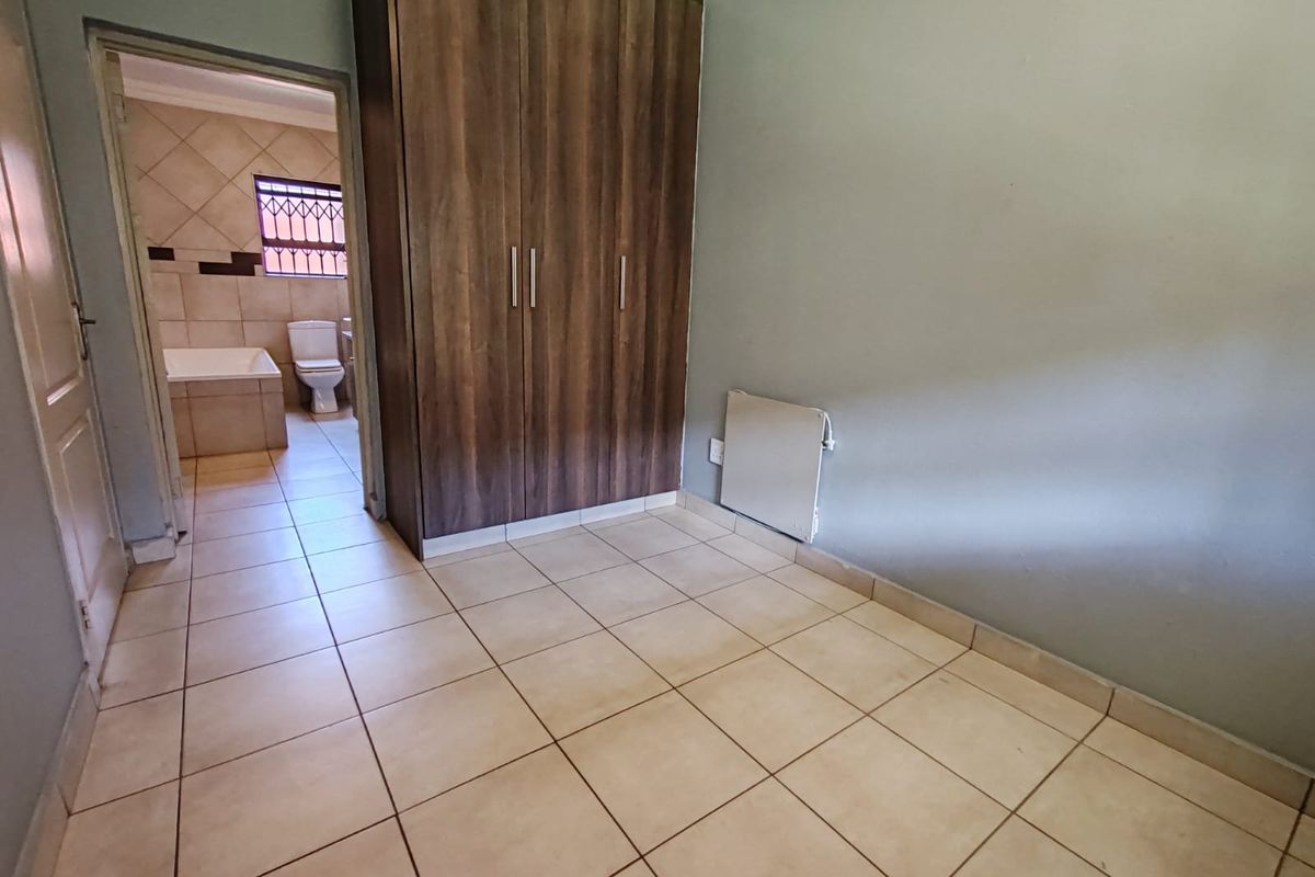 A bedroom featuring tiled flooring and built-in wooden cupboards, with an adjacent en-suite bathroom visible through the doorway.