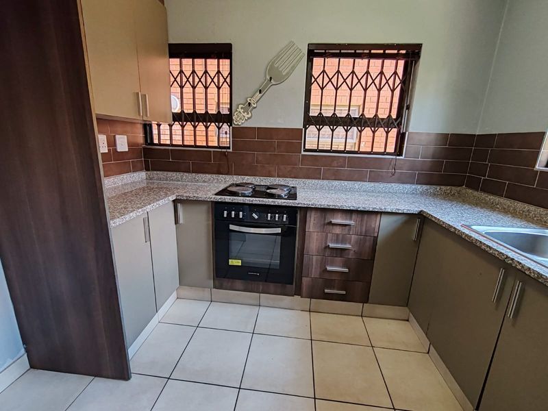 A functional kitchen featuring granite countertops, built-in oven and hob, tiled backsplash, and ample storage cabinetry with secure window bars.