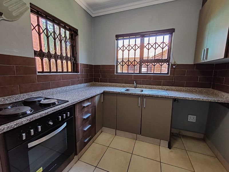 A functional kitchen featuring built-in cabinetry, a stove with electric hob, laminate countertops, and tiled finishes with security bars on the windows.