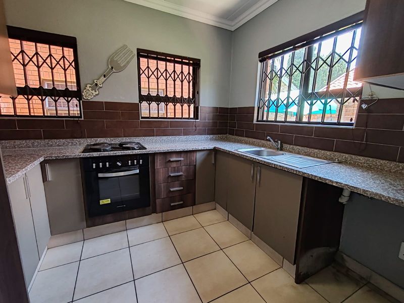 A functional kitchen featuring built-in cabinetry, a hob, an oven, tiled splashbacks, and tiled flooring, with security bars installed on the windows.